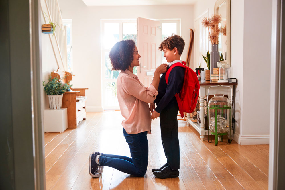 A young boy's mum knelt down in the hallway straightening his tie