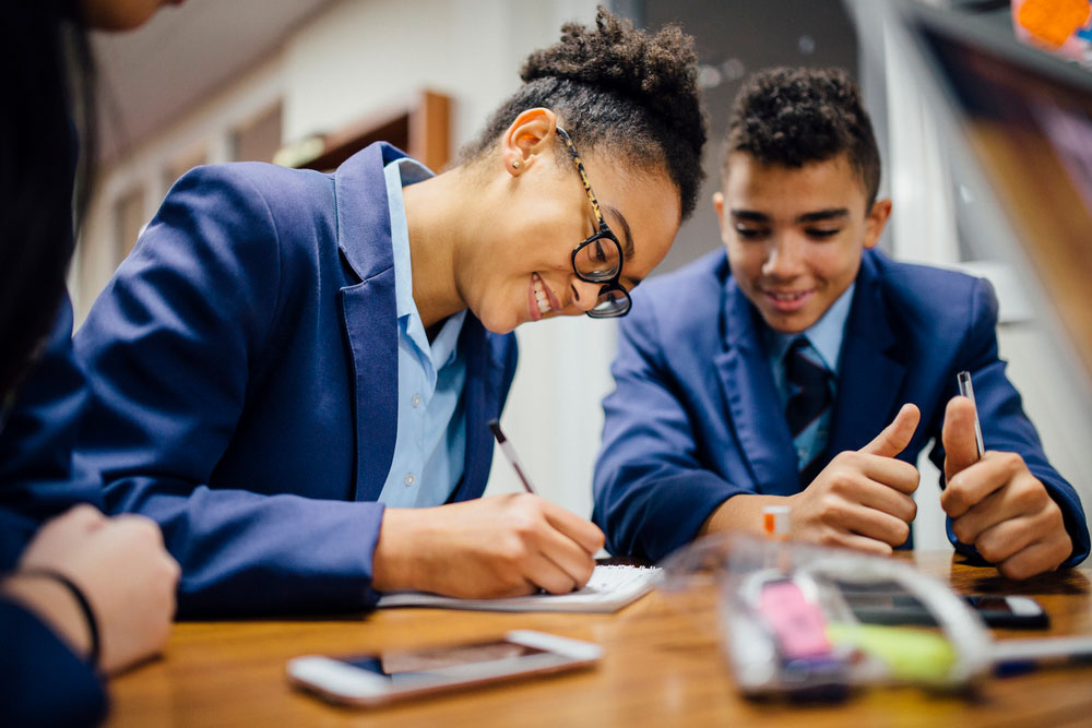 Three school students sat at a desk writing down notes