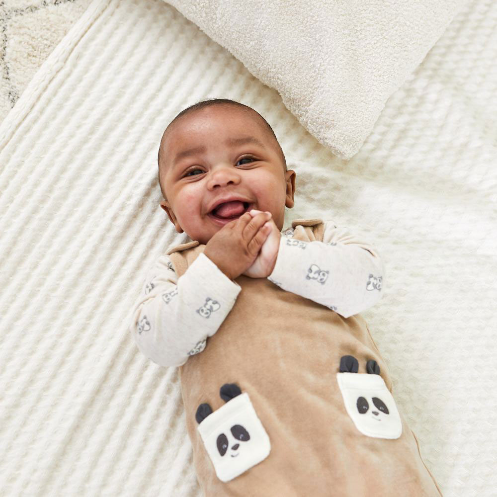 A baby laid on a mat wearing a baby suit with panda print