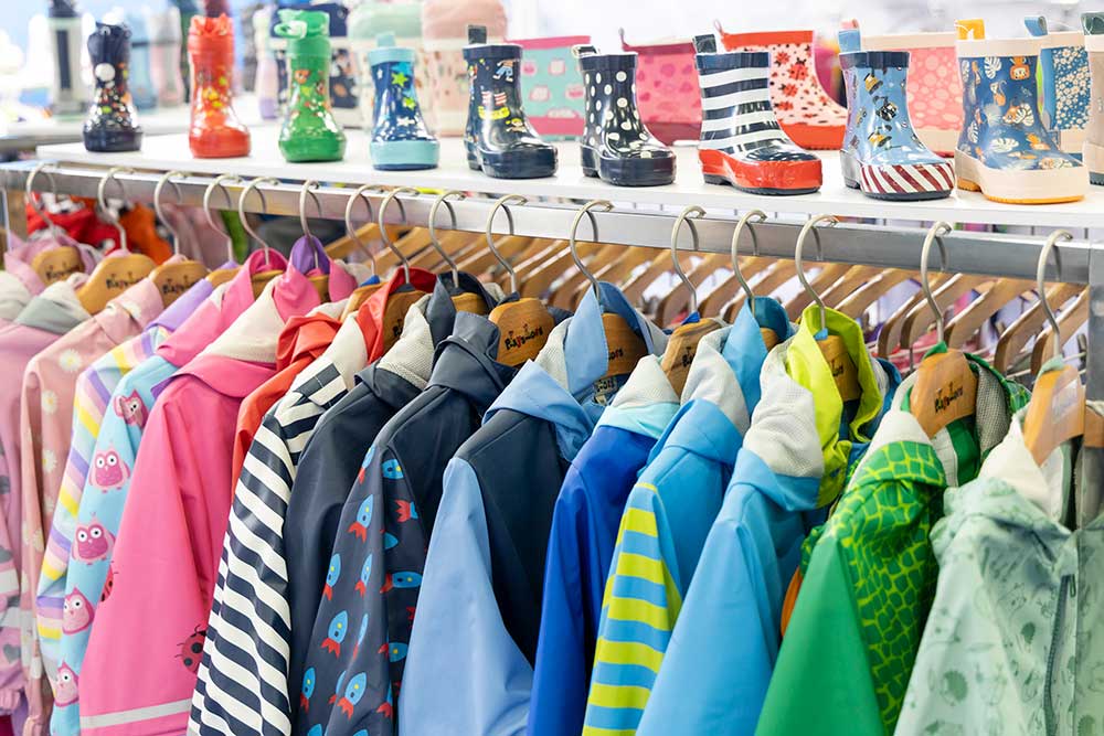 Children's jackets hung up on a rail with wellington boots stood on top of the shelf