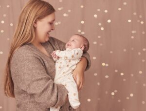 A woman holding a baby wearing a gingerbread man rented babygro from Borro