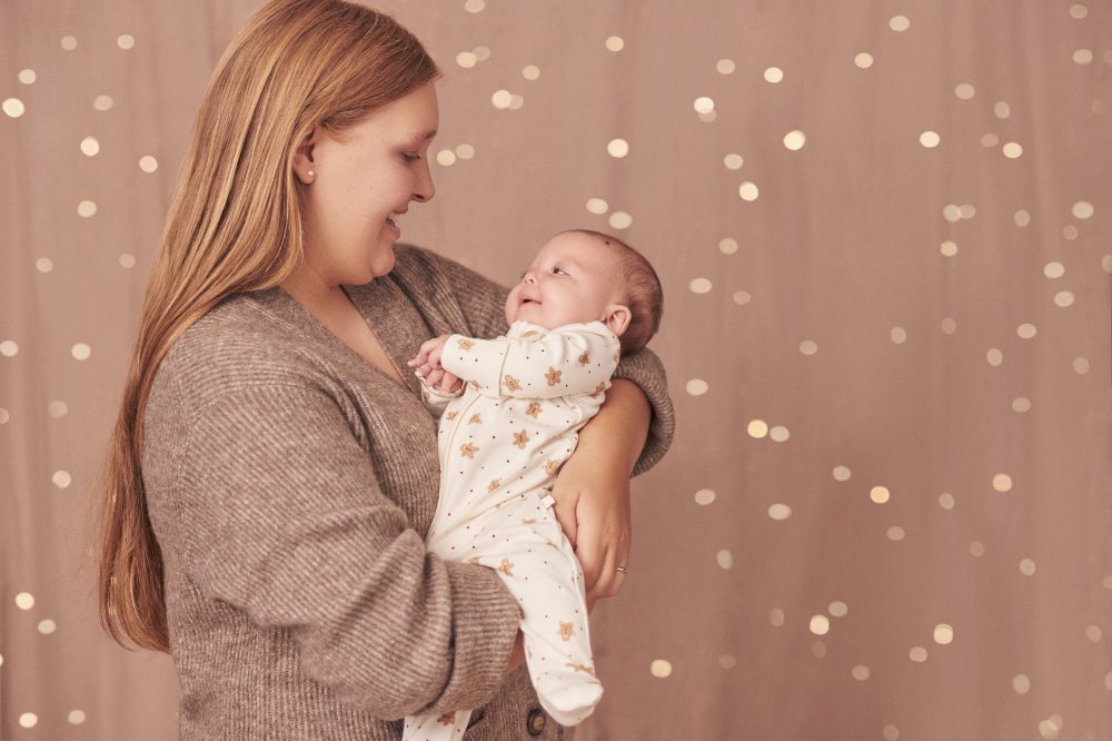 A woman holding a baby wearing a gingerbread man rented babygro from Borro