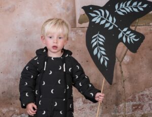 A young boy wearing a moon print onesie by Organic Zoo x Toastie