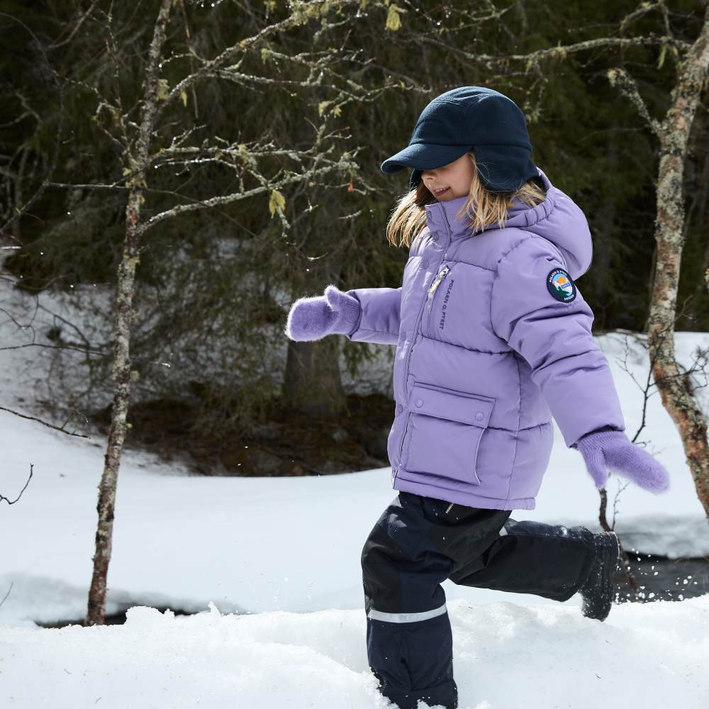 A young girl walking outside in the snow wearing a hat, lilac jacket and trousers from the PO.P On Adventure Ski Edition collection