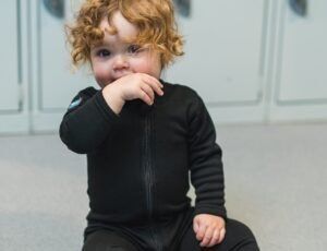 A young child sat on the floor wearing the new black Thermaswim children’s wetsuit by Splash About