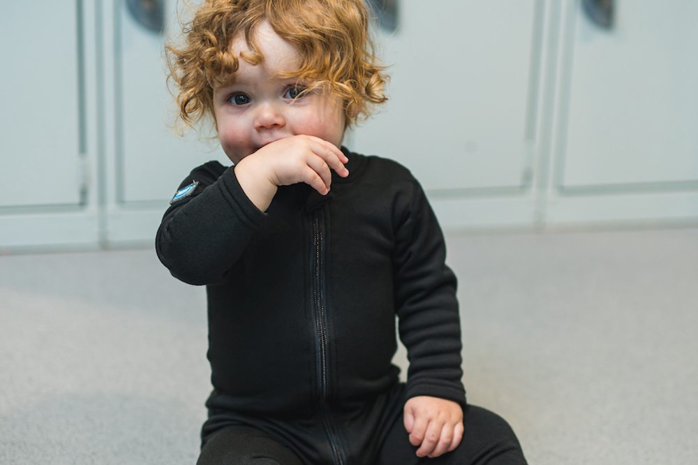 A young child sat on the floor wearing the new black Thermaswim children’s wetsuit by Splash About