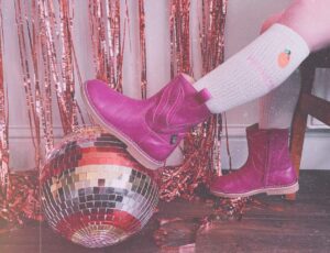 A child in pink cowboy boots resting their feet on a disco ball