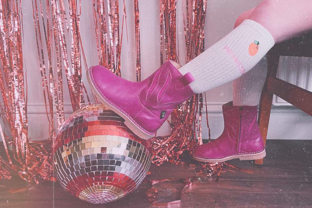 A child in pink cowboy boots resting their feet on a disco ball