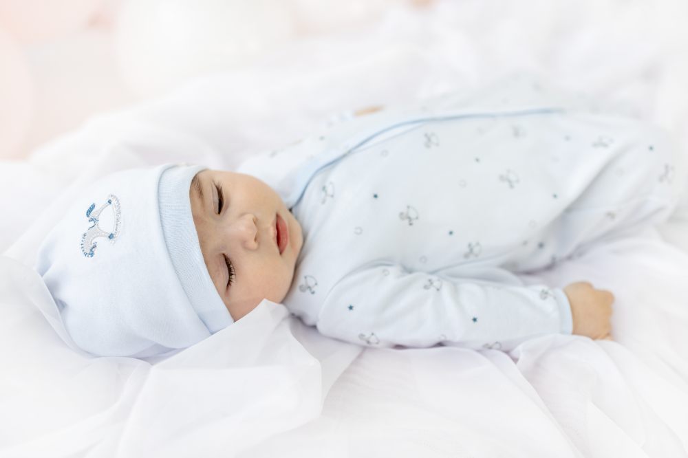 A young baby lying on their back wearing a pale blue hat and matching babygro