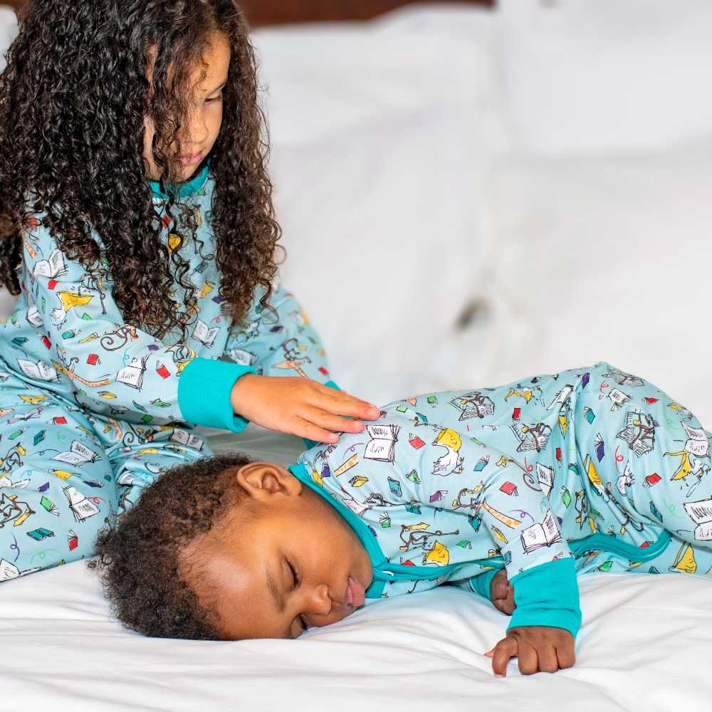 A young girl and a baby on a bed wearing sleepwear from the Ducky Zebra x Roald Dahl collection 