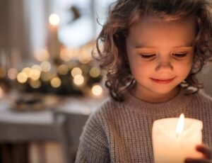 A young girl holding a candle in a candle lit room representing FTCT's Winter Appeal