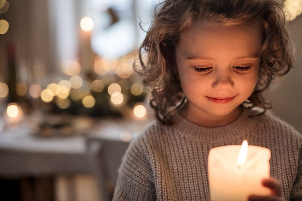 A young girl holding a candle in a candle lit room representing FTCT's Winter Appeal