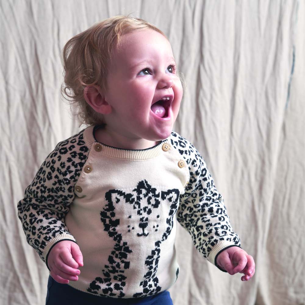 A young child smiling wearing a knitted jumper with a leopard motif on the front