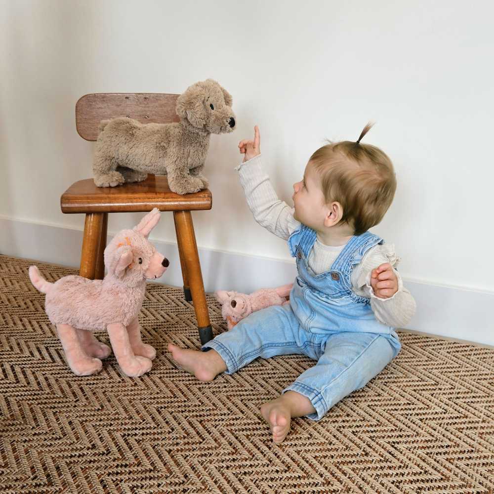 A young child sat on the floor leaning over to a chair with a pink and brown plush dog on 