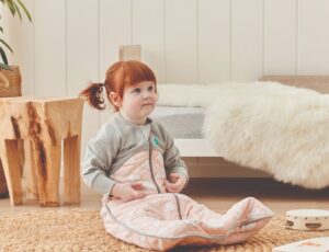 A young girl with red hair sat on the floor in a sleeping bag by Love to Dream