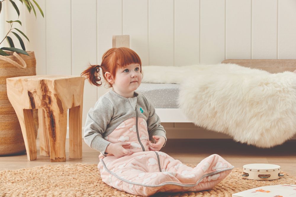 A young girl with red hair sat on the floor in a sleeping bag by Love to Dream