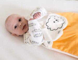 A baby lying down in a hippo print babygro and a yellow sleeping bag by Pure Earth Collection