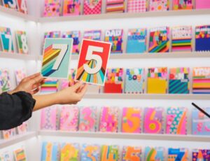 Someone's hands shown holding up some greeting cards in front of shelves of cards