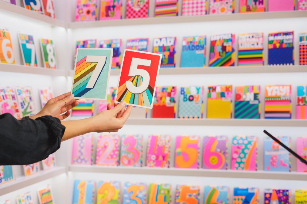 Someone's hands shown holding up some greeting cards in front of shelves of cards