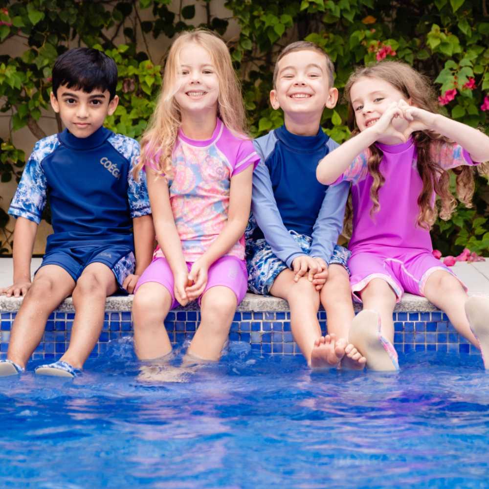 Four children in swimwear sat at the edge of a swimming pool