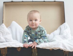 A baby in a vintage suitcase wearing an acorn print babygro by Pigeon Organics