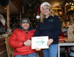 A man shaking a woman's hand who is holding a certificate on a Christmas stand on Small Business Saturday