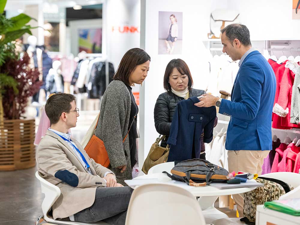 Buyers stood on a stand with an exhibitor looking at clothing samples