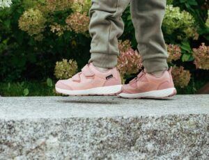 A young girl in pink and white trainers walking along the top of a wall