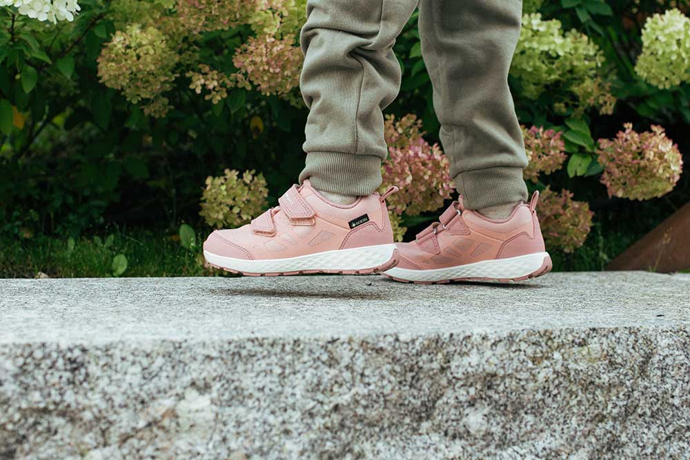 A young girl in pink and white trainers walking along the top of a wall