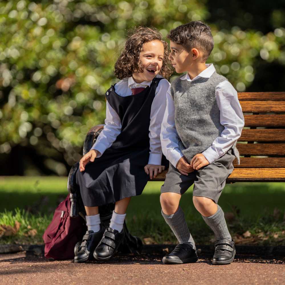 Two children in school uniform sat outside on a bench 