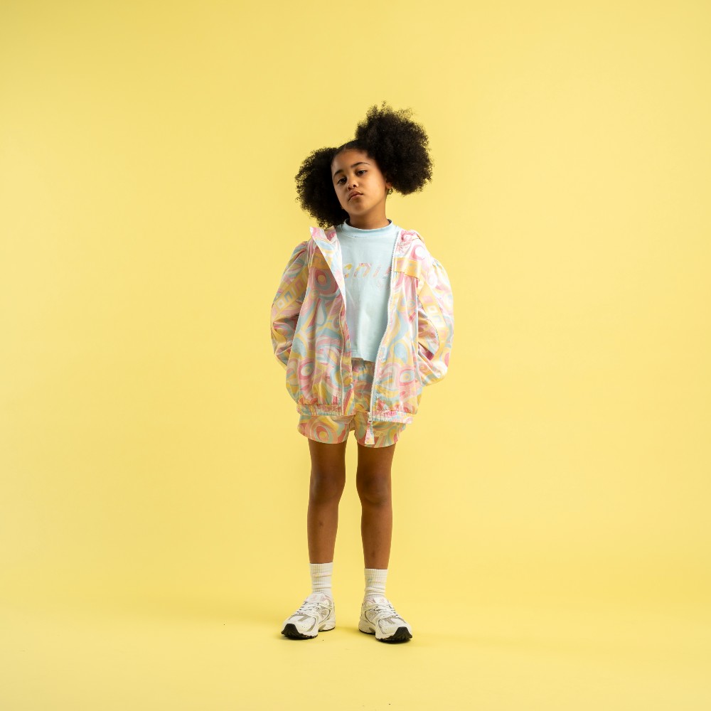 A girl stood against a yellow background wearing a tracksuit top and shorts by Bonini 