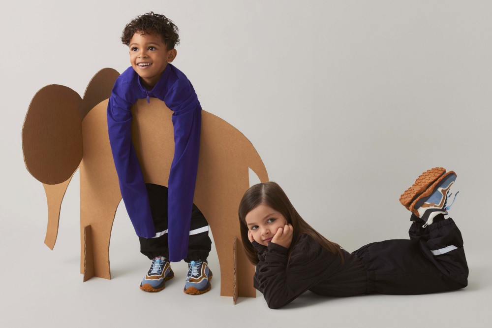 A boy leaning on a cardboard elephant beside a girl lying on the floor on her front 