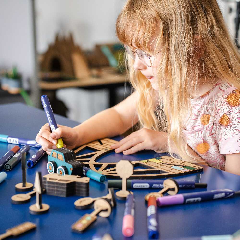 A girl sat at a blue desk colouring in beside a selection of toys by Crateit