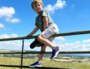 A young boy in shorts, T-shirt and trainers sat on a gate in a field