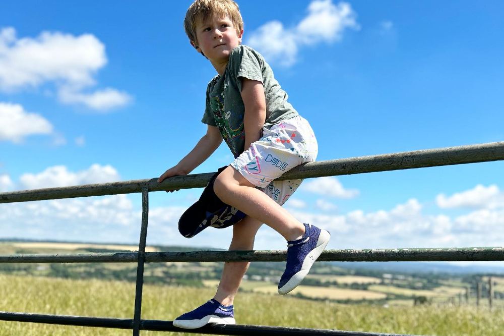 A young boy in shorts, T-shirt and trainers sat on a gate in a field