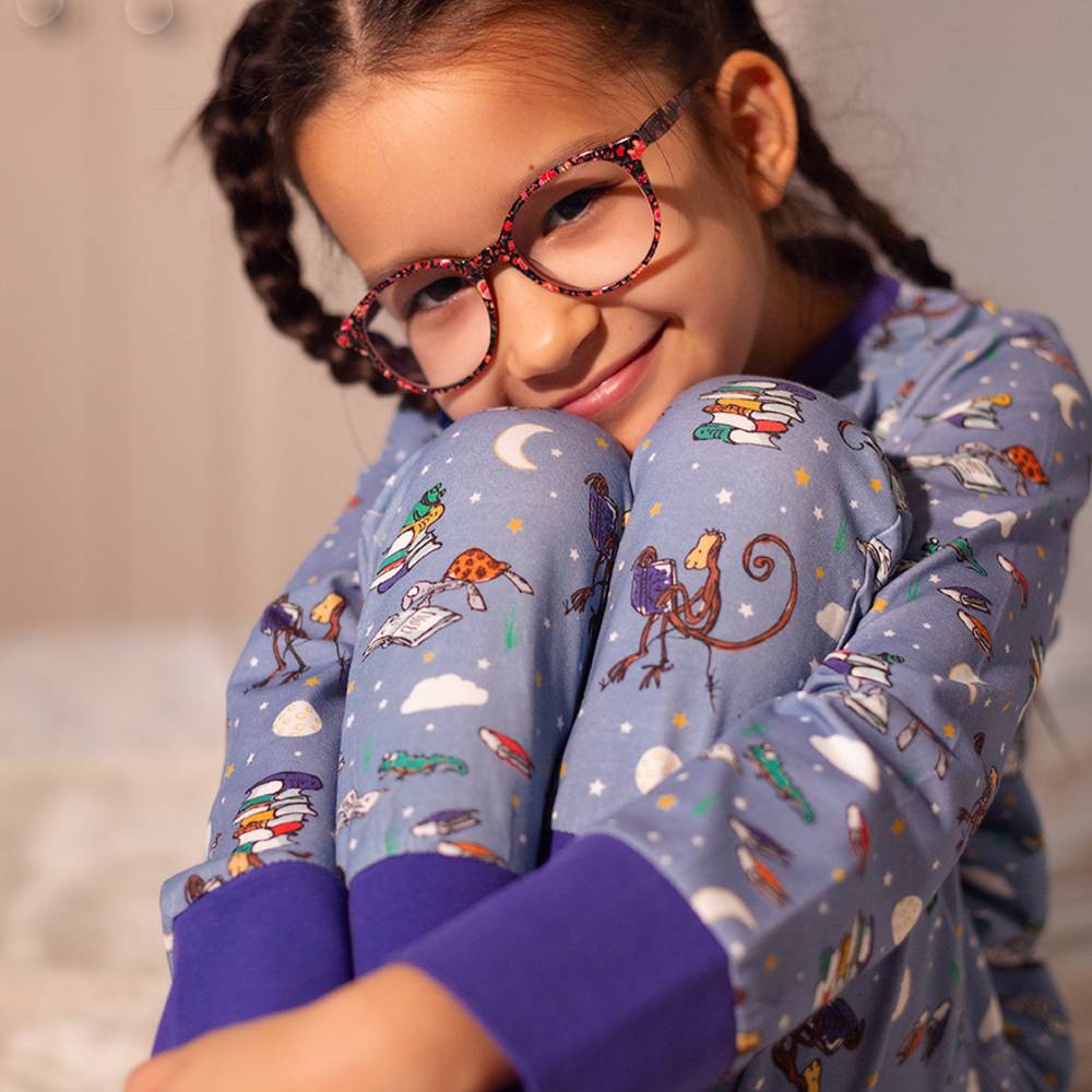 A young girl in glasses wearing a pair of purple pyjamas with a Roald Dahl print 