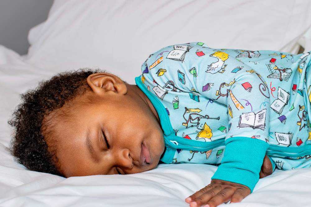 A young child sleeping wearing a turquoise sleepsuit with a Roald Dahl print 