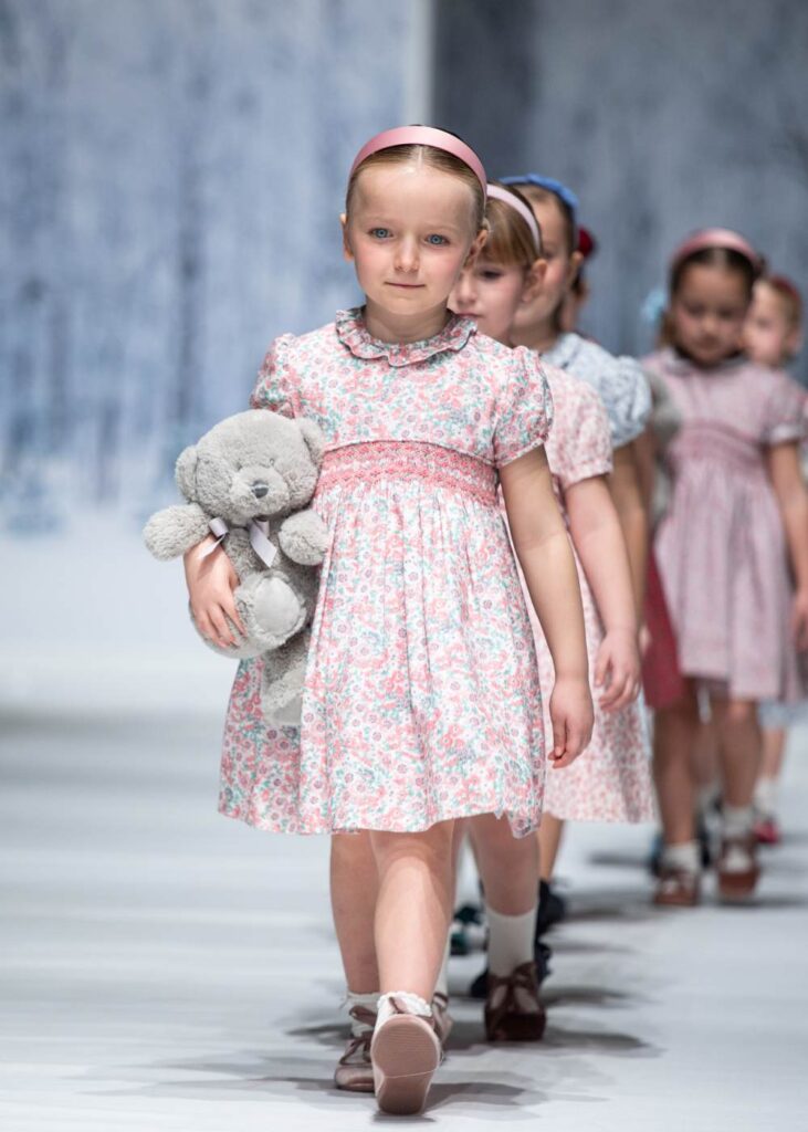 A row of girls in traditional floral dresses walking down a catwalk 