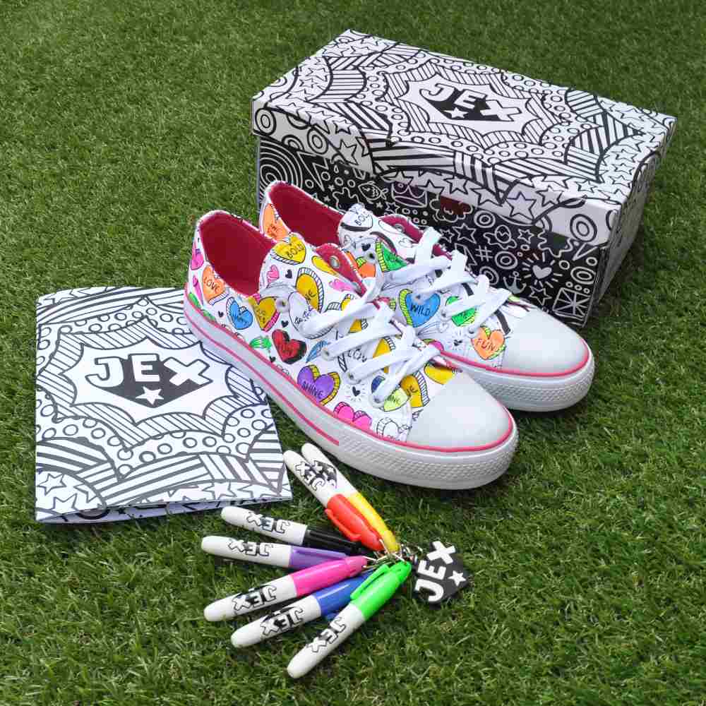 A pair of child's colour-in trainers on grass beside pens, a shoebox and a notepad 