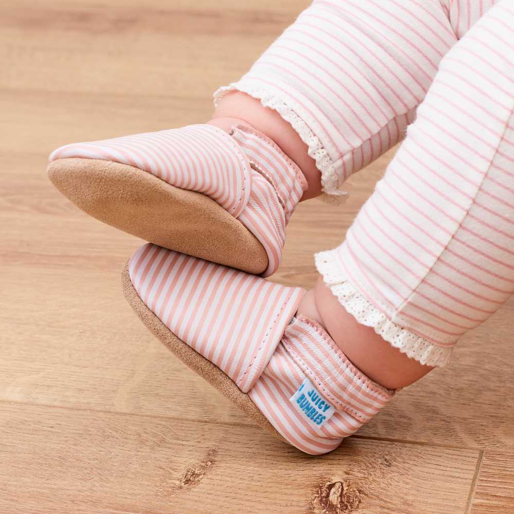 A baby's feet wearing pink soft soled shoes and pink and white striped leggings