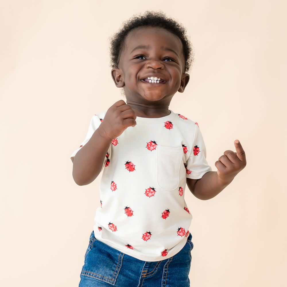 A young child smiling wearing a white T-shirt with ladybugs on and blue jeans