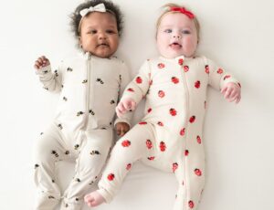 Two babies lying side by side wearing a babygros with bees and ladybugs on by Kyte Baby