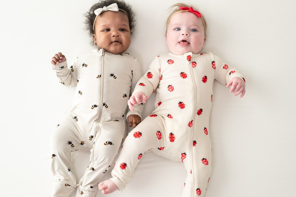 Two babies lying side by side wearing a babygros with bees and ladybugs on by Kyte Baby