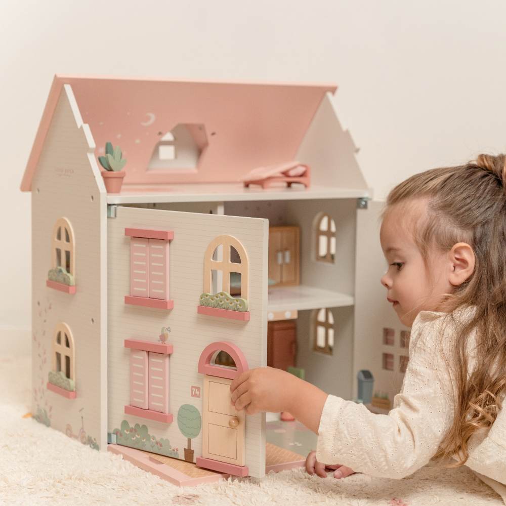 A young girl lying on her front playing with a large dolls' house 