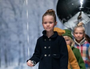 A row of children walking down a fashion catwalk holding silver balloons