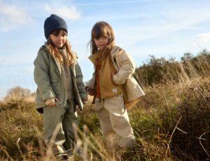 Two girls stood outside in long grass wearing outwear clothing