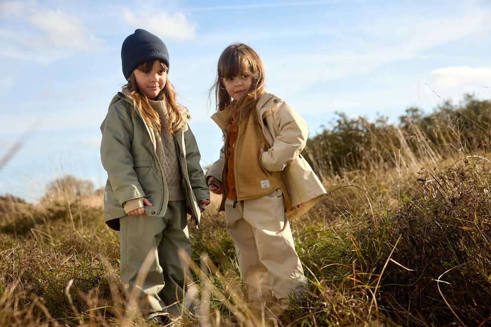 Two girls stood outside in long grass wearing outwear clothing