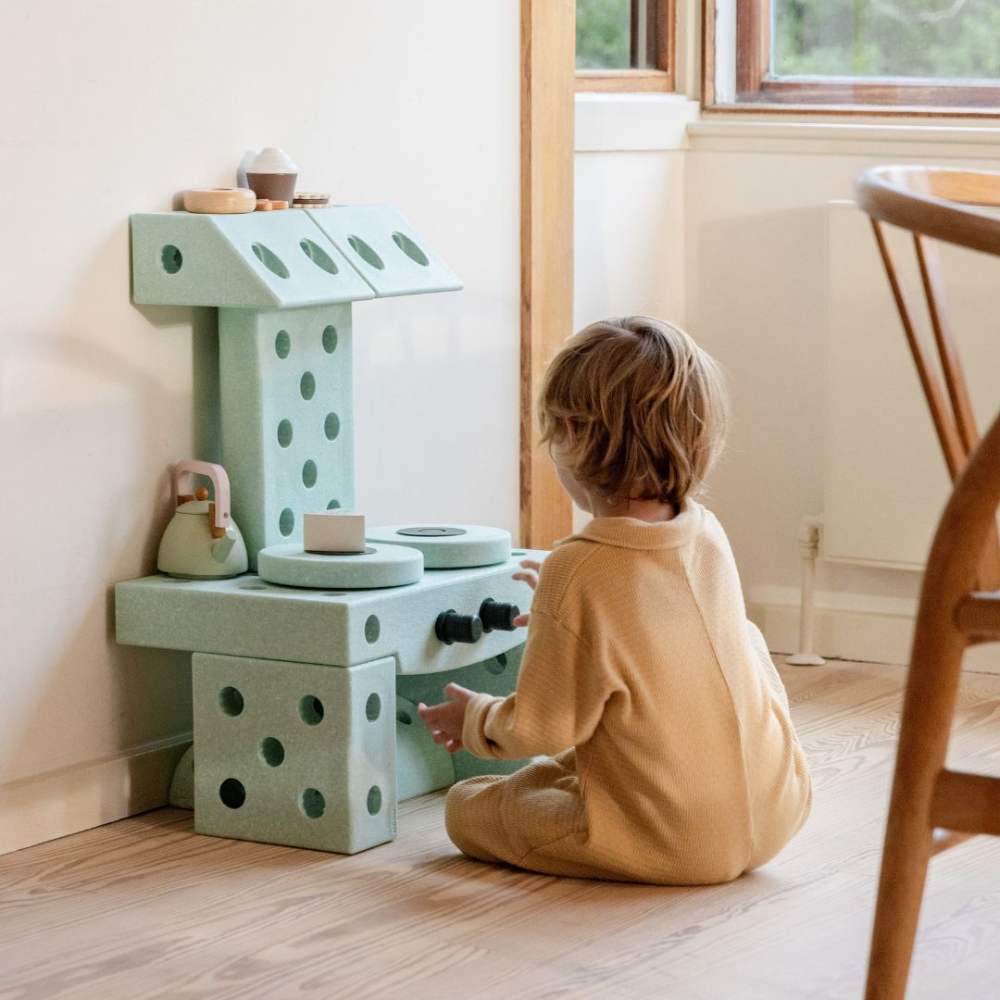 A child sat on the floor in a room playing with a play kitchen made out of MODU blocks 