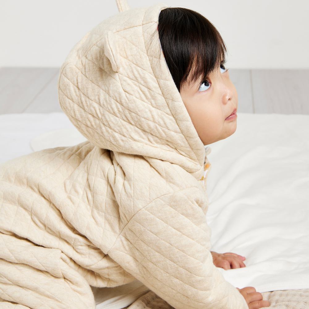 A baby crawling wearing a cream hooded babygro with ears 