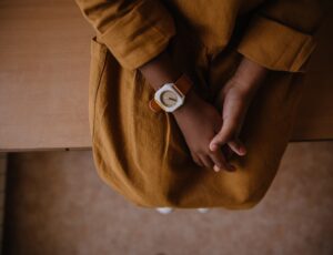 A child sat on a wooden seat in a mustard coloured dress wearing a watch